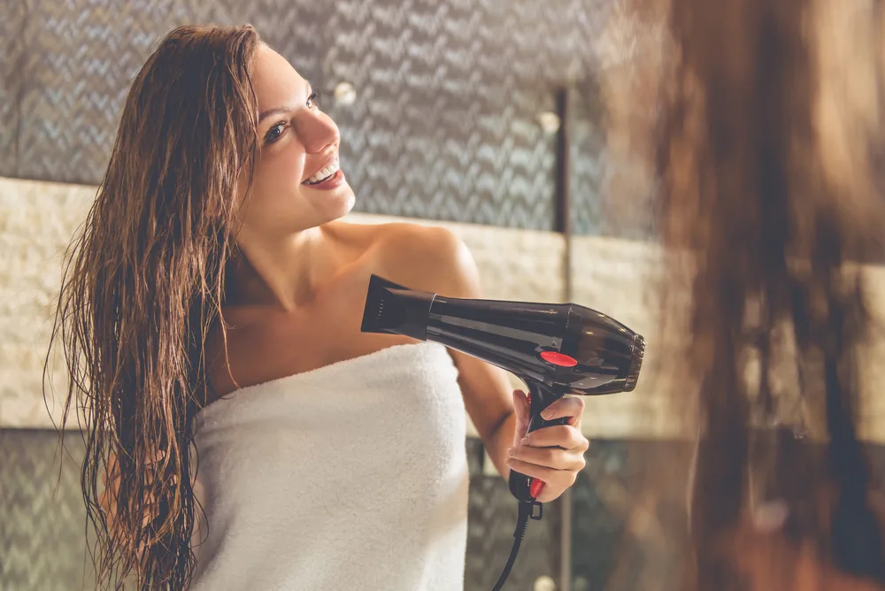 Woman in a towel in a rustic looking bathroom for a piece on the best hair dryer for straightening your hair