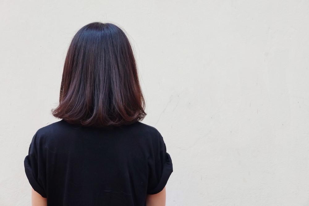 Woman seen from back wearing black t-shirt models shoulder-length dark brown hair with maroon balayage