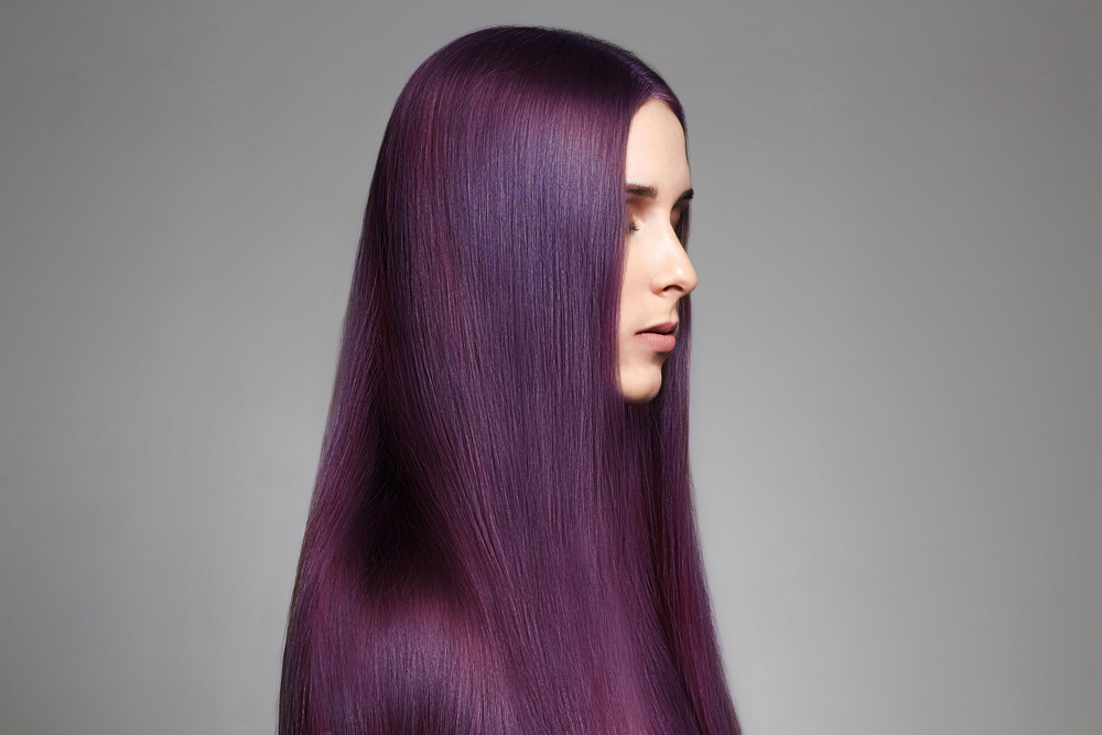 Woman facing to the right with very long straight hair shows off her dark purple hair color with an oil slick look