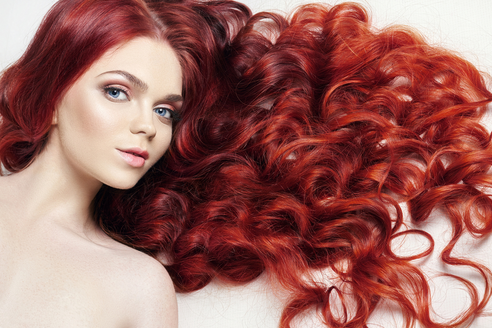 Woman lies with curly hair scattered around her on a white surface with a warm red ombre hair color