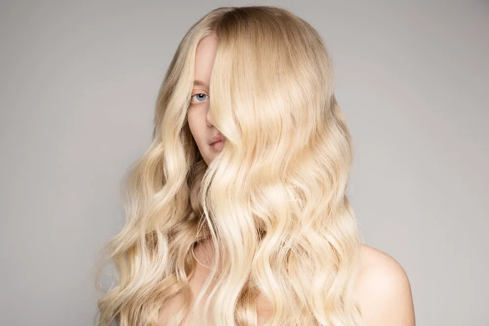 Blonde-haired woman peeks through her hair styled in medium beach waves done in a retro glam style