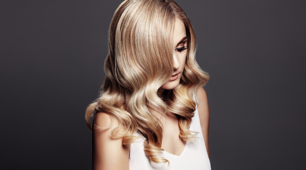 Woman looks down on dark gray background with dimensional honey blonde as one of the best hair color for dirty blondes