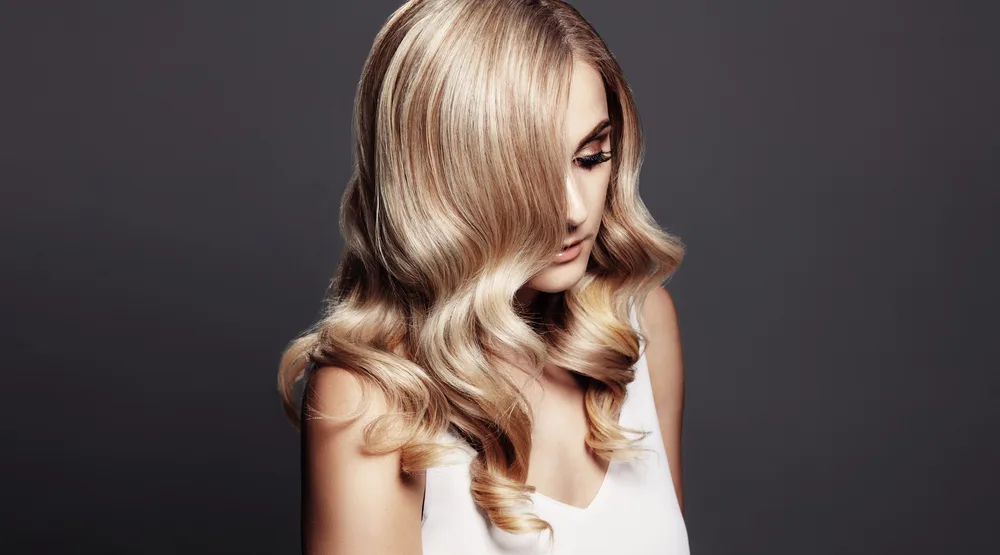 Woman looks down on dark gray background with dimensional honey blonde as one of the best hair color for dirty blondes