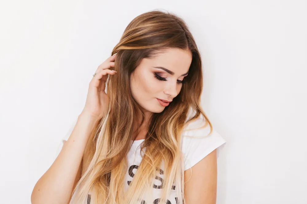 Woman looks down with honey blonde highlights in brown hair as the best hair color for dirty blondes