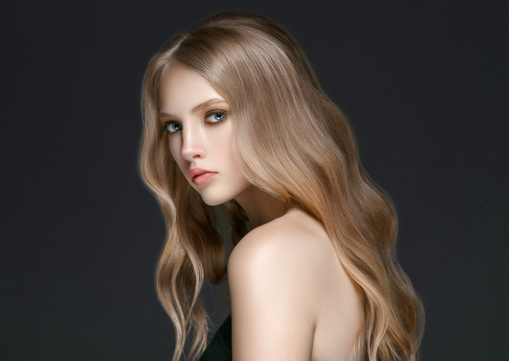 Woman with dark blonde hair shows off medium beach waves in a trendy flattened style against black background