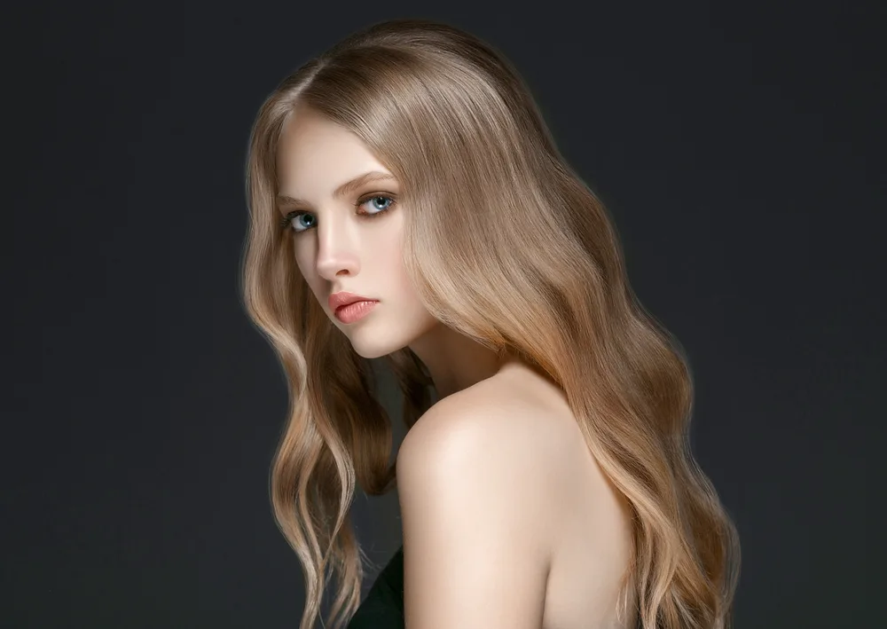 Woman with dark blonde hair shows off medium beach waves in a trendy flattened style against black background