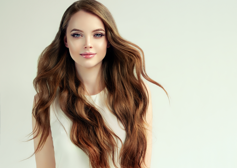 Brunette woman with long medium beach waves hair style smiles with her hair flowing over her shoulders in white dress