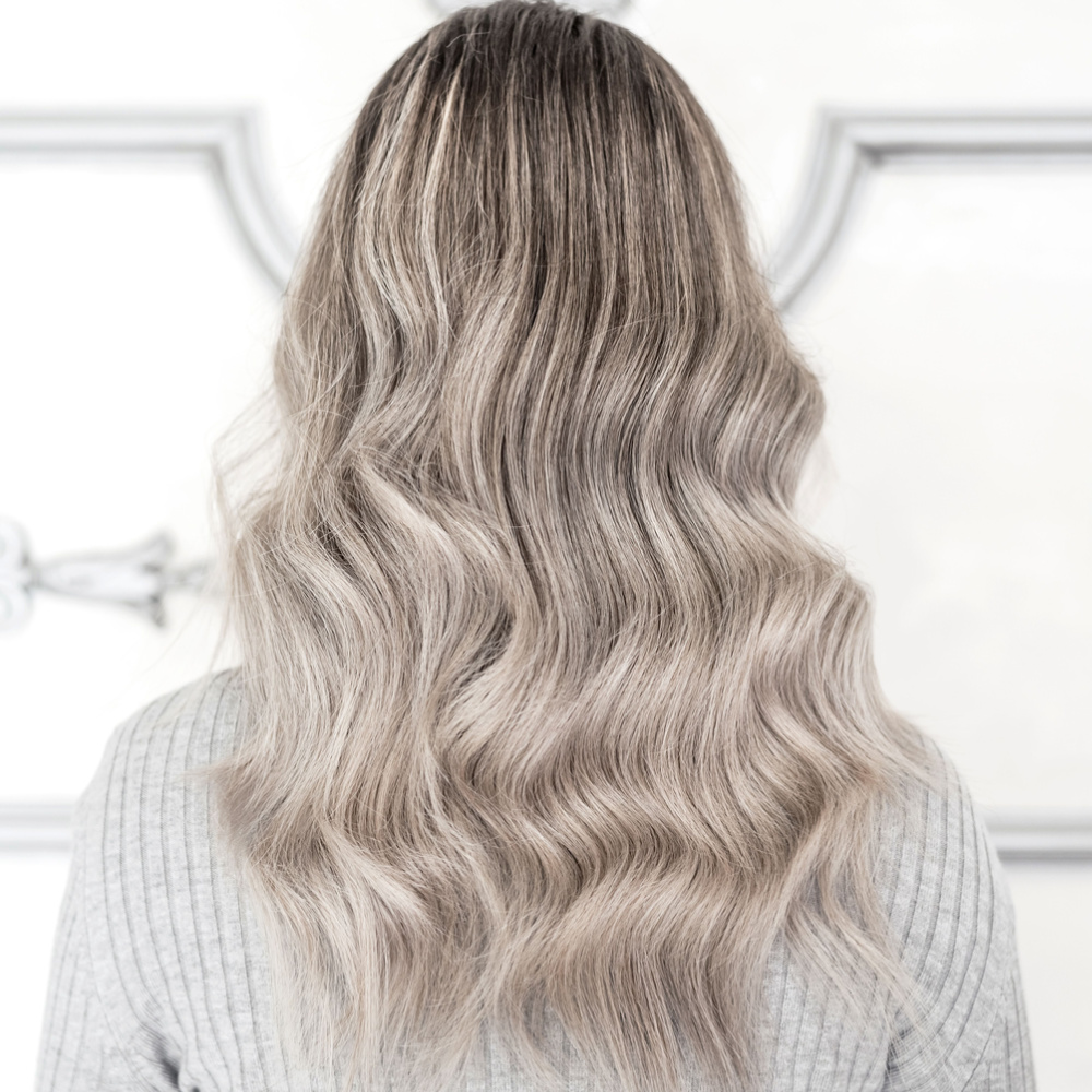 Back view of woman with wavy light ash blonde hair wearing gray sweater