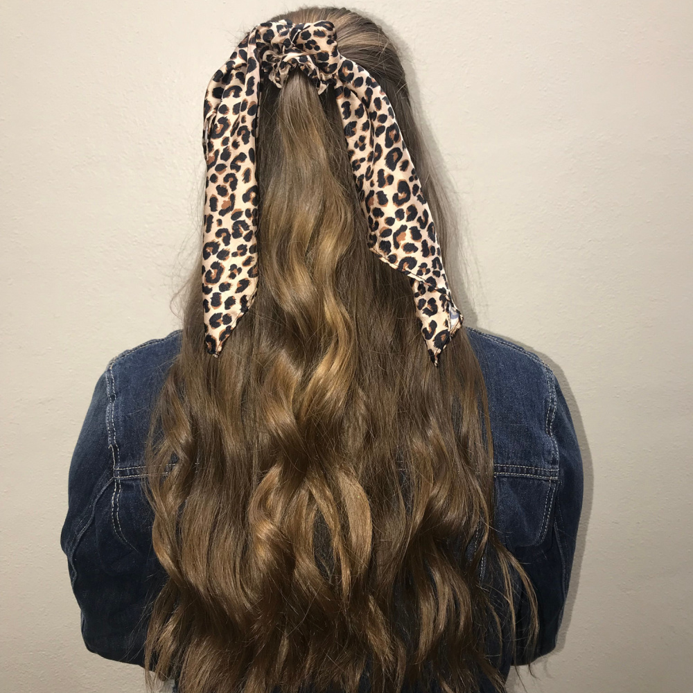 Rear view of woman's long wavy hair in a half up ponytail secured with a leopard scrunchy scarf