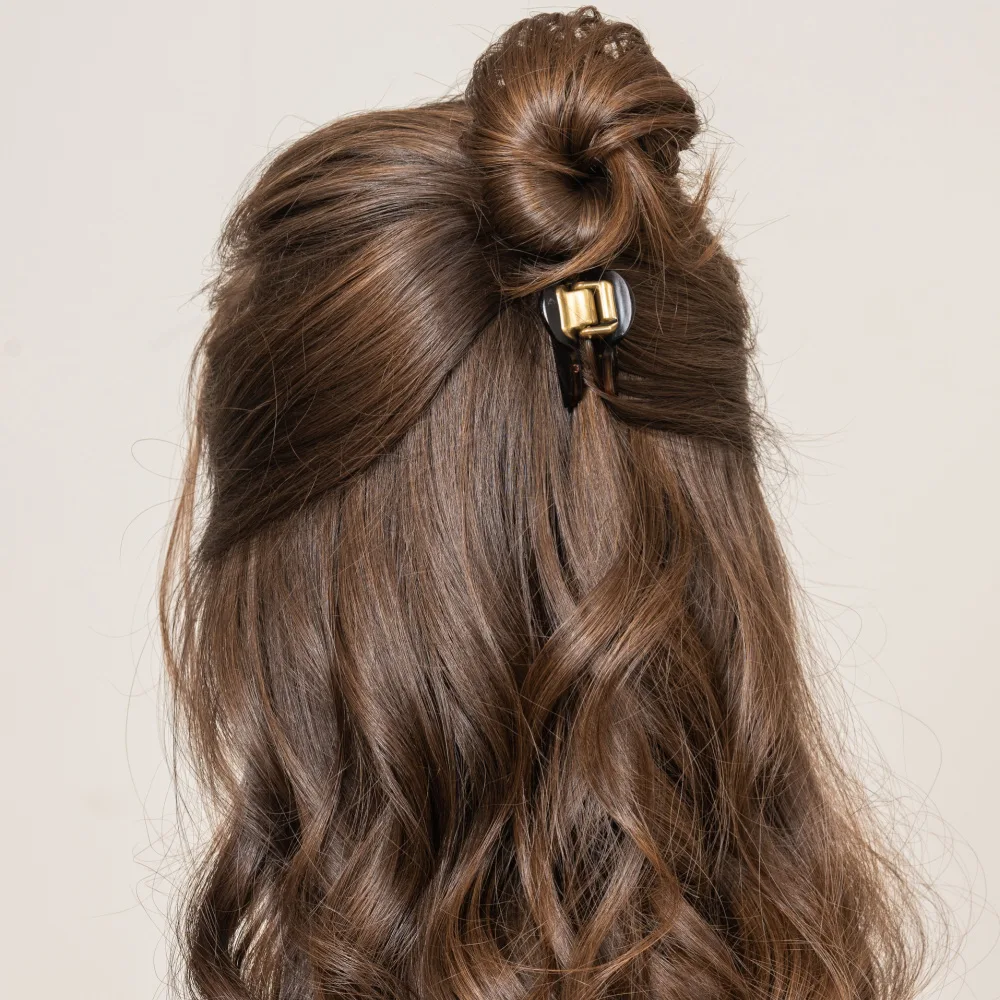 Back view of woman with long curly brunette hair wearing one of many cute half up half down hairstyles with a hair clip and bun