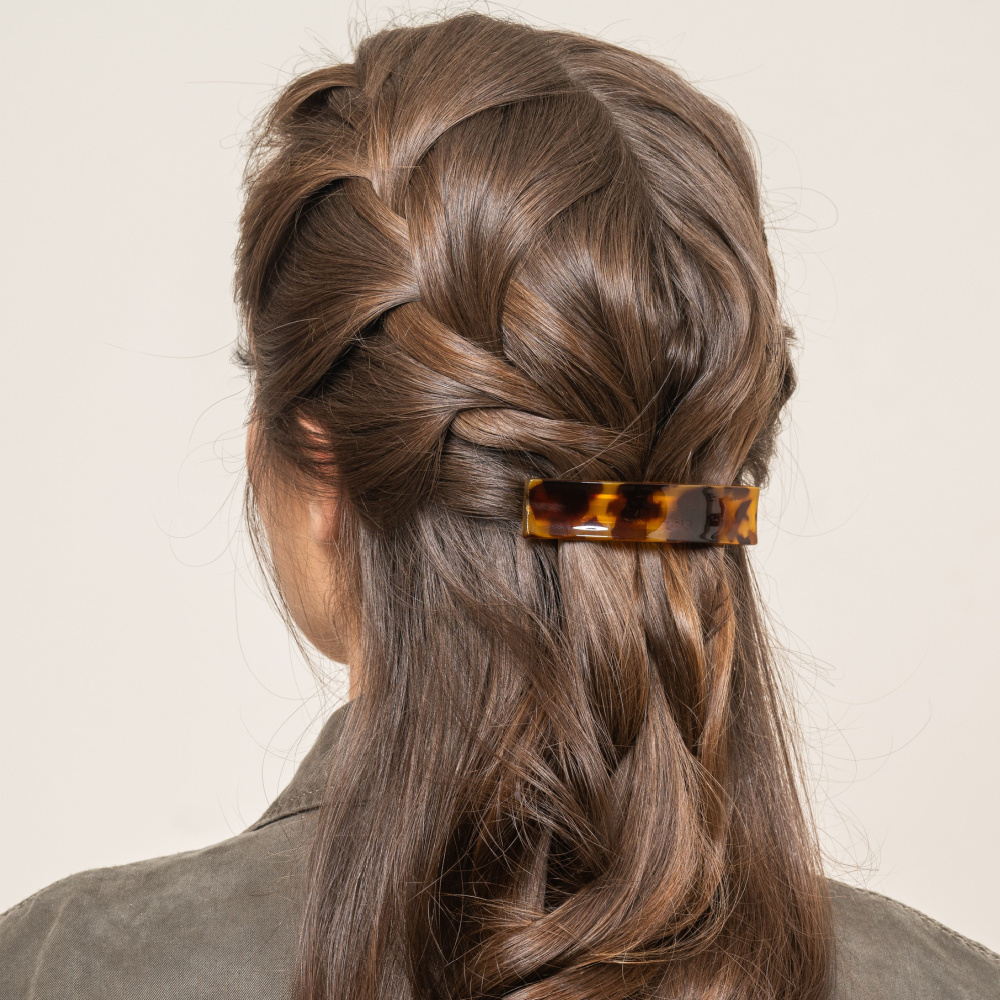 Long curly brunette hair shown from rear with French braids half up hairstyle and hair barrette