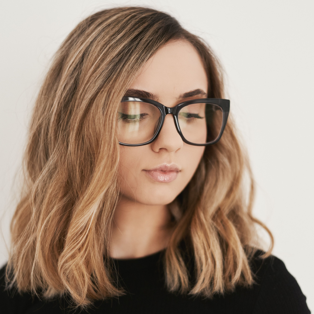 Blonde woman with glasses wears one of the best heart shaped face haircuts with a long bob styled with waves and a side part