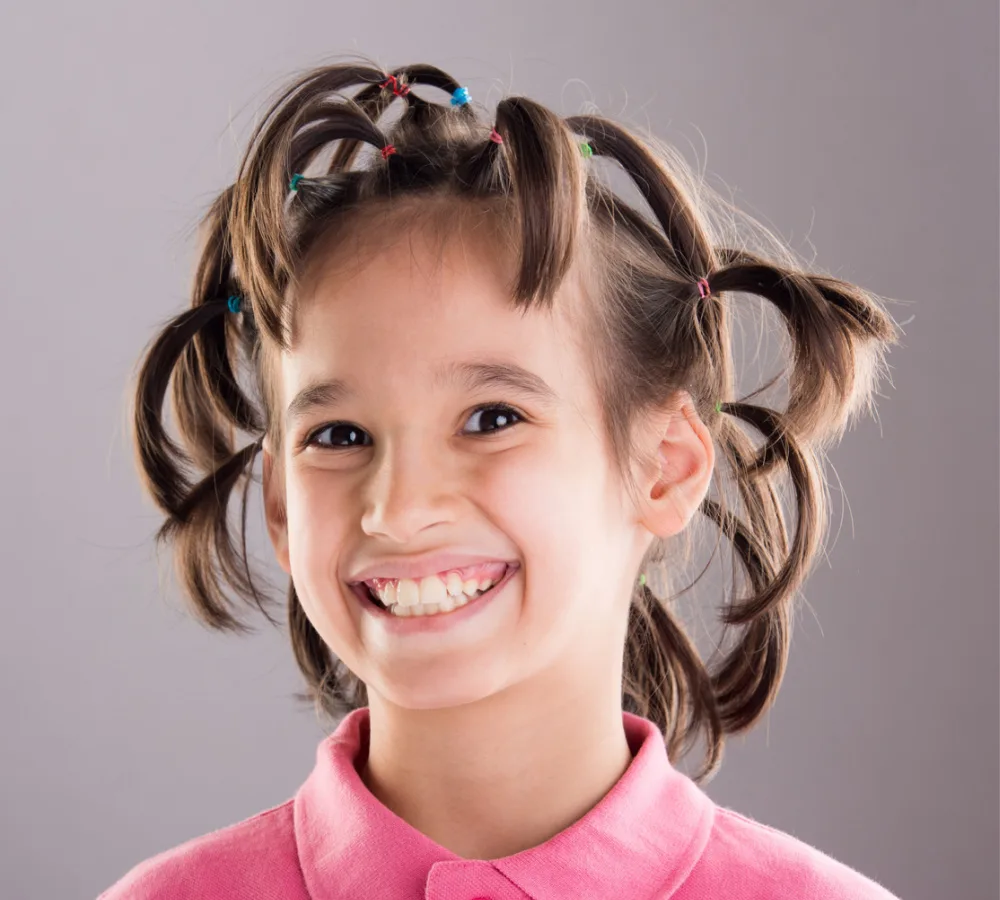 Little girl in pink collared shirt wears lots of pigtails for a piece on crazy hair day ideas