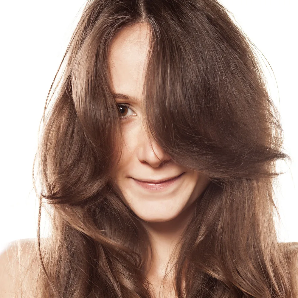 Close up of woman with brunette long hair in a shag haircut smiling with her bangs in her face