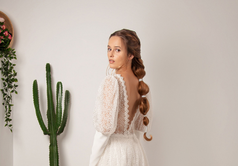 Woman in wedding gown looks over her shoulder while wearing a bubble braid hairstyle down the back with cactus on her left