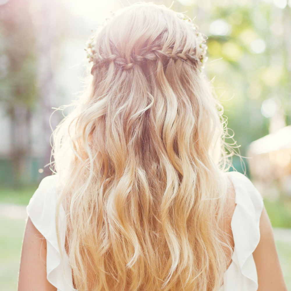 Blonde bride in white dress wears her long wavy hair in a half up half down style with waterfall braid