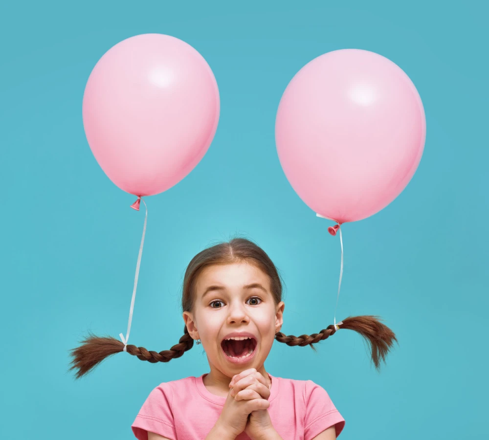 Little girl in pink t-shirt wears braids with pink balloons attached for a piece on crazy hair day ideas 