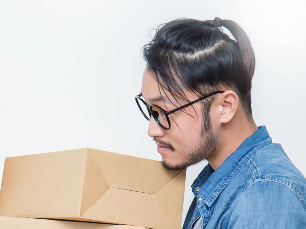 Man lifting boxes wears a denim shirt and half up half down man bun hairstyle with long hair