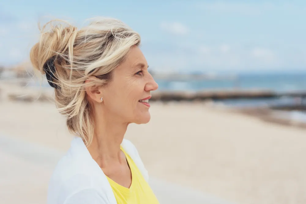Beachy casual updo on a woman on the beach wearing a yellow shirt and a white cardigan