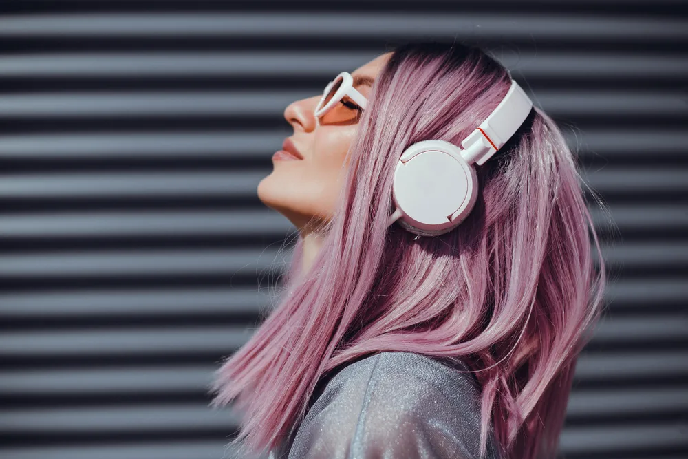 Frosty mauve light pink hair on a woman wearing headphones and throwing her head back and looking upward through her sunglasses