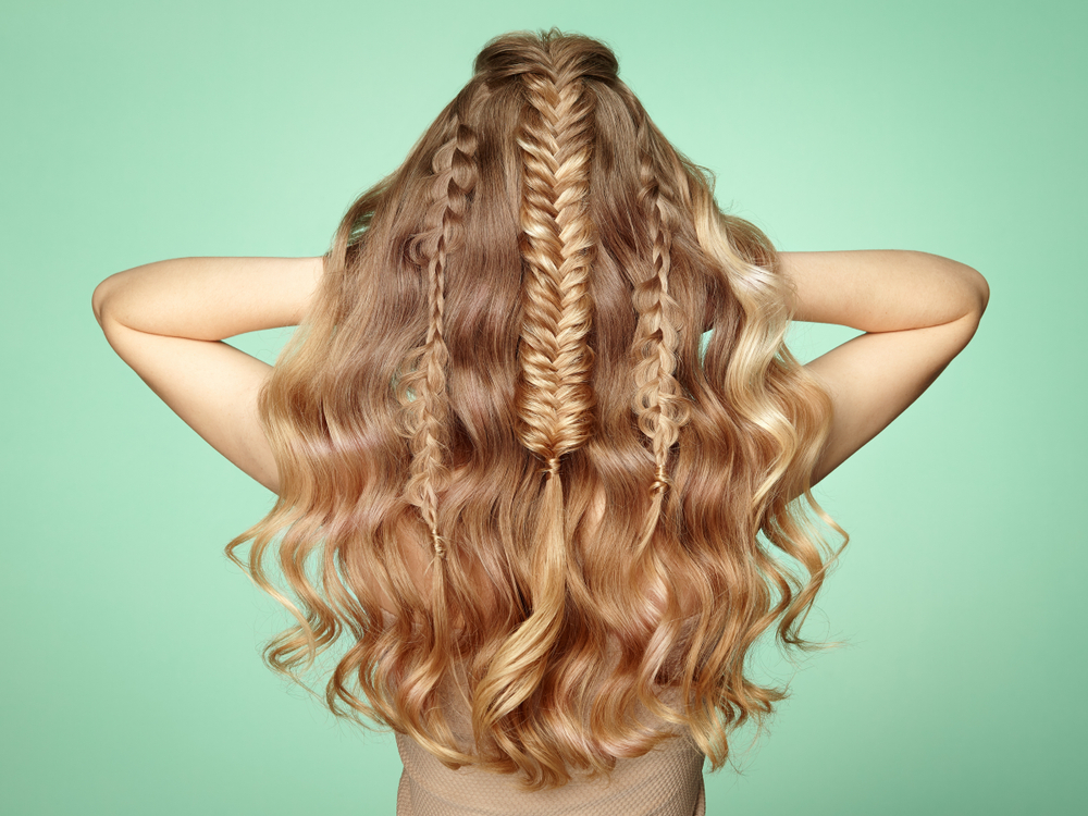 Back view of woman wearing one of the prettiest half up half down hairstyles with braids posing with arms raised in front of pastel green wall