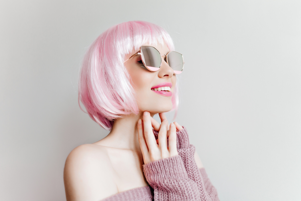White Taffy Pink Blonde pictured with her hands below her chin smiling and looking up through her sunglasses