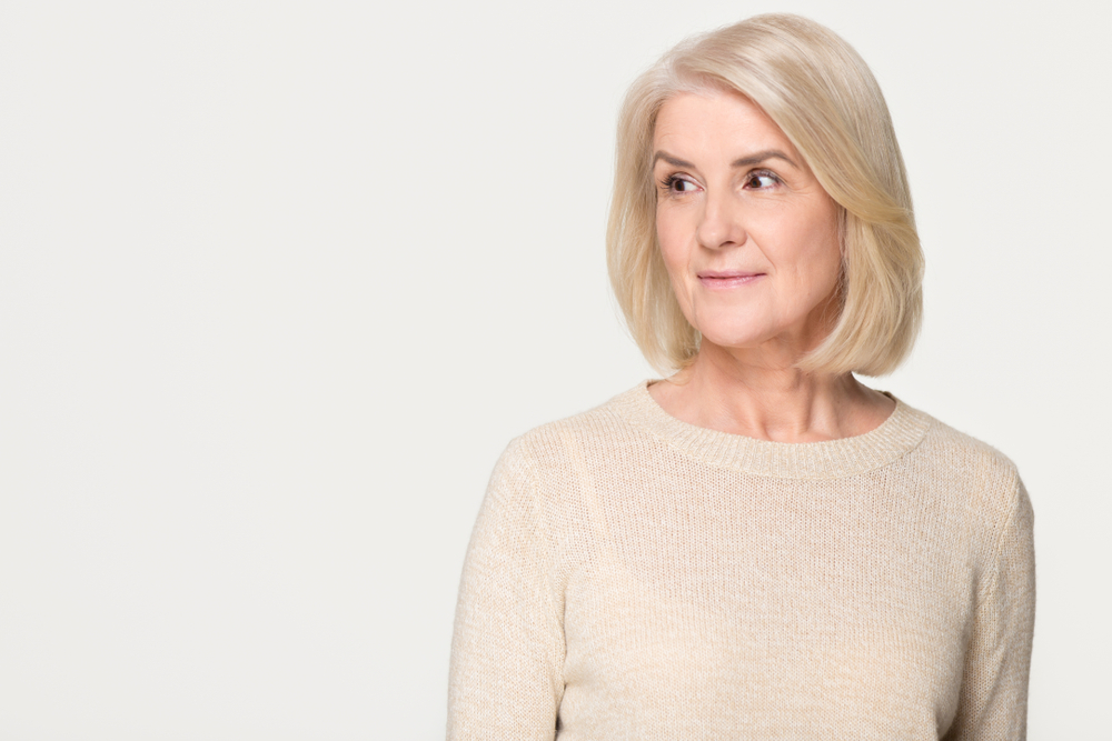 For a roundup of the best medium-length layered hairstyles for women over 50, a woman wears a Feathered Back Face-Framing Layers
