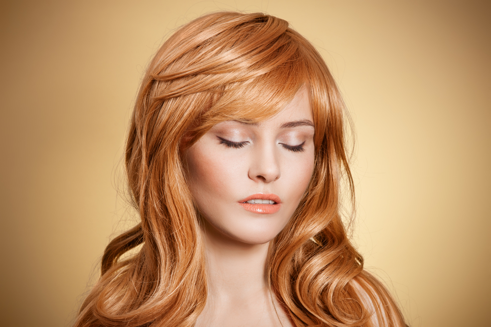 Woman with red hair closes her eyes in front of golden background wearing one of the long shag haircuts of the 1960s