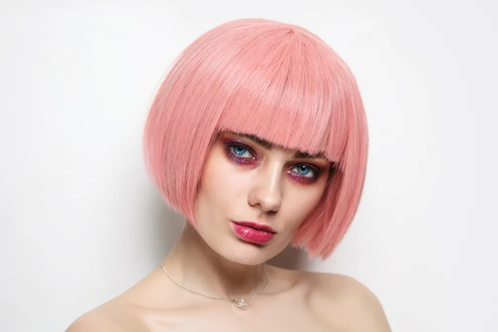 Woman with light coral rose colored hair and pale skin with red lipstick in a white room tilting her head