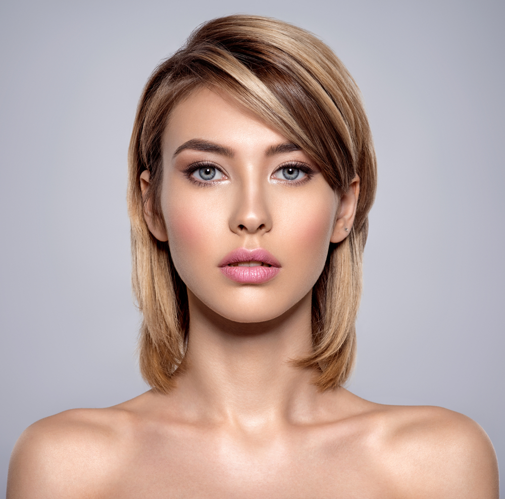 Long Layered Bob With Side Bangs on a woman with a bare clavicle in a model's pose in a grey room
