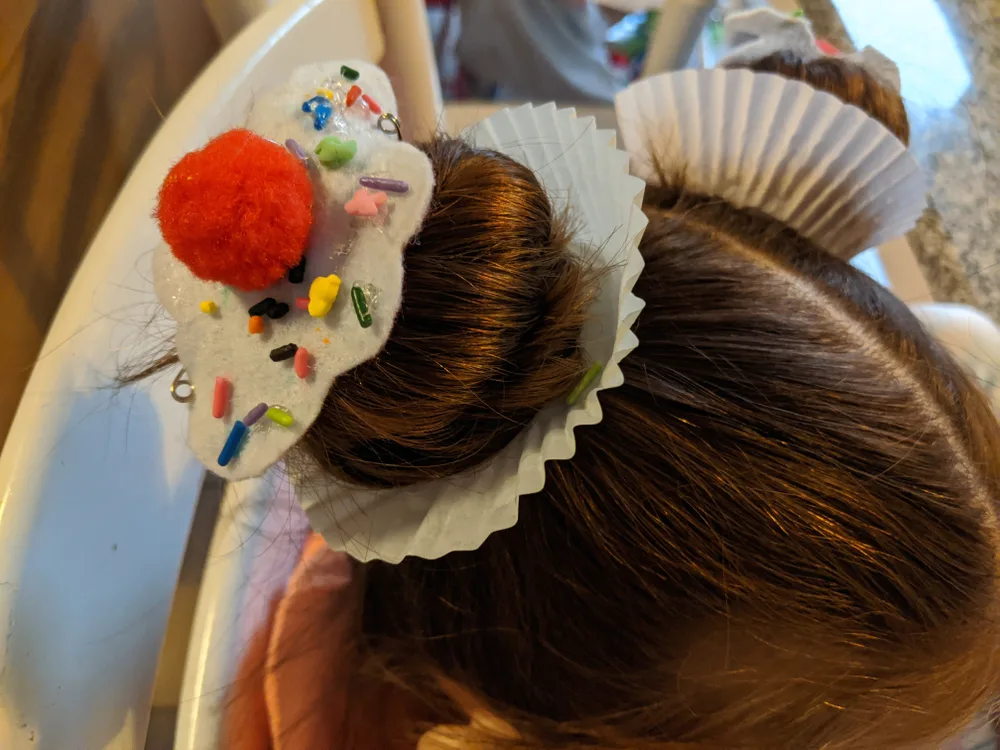 Little girl wears cupcake space buns as an example of crazy hair day ideas with cupcake wrappers