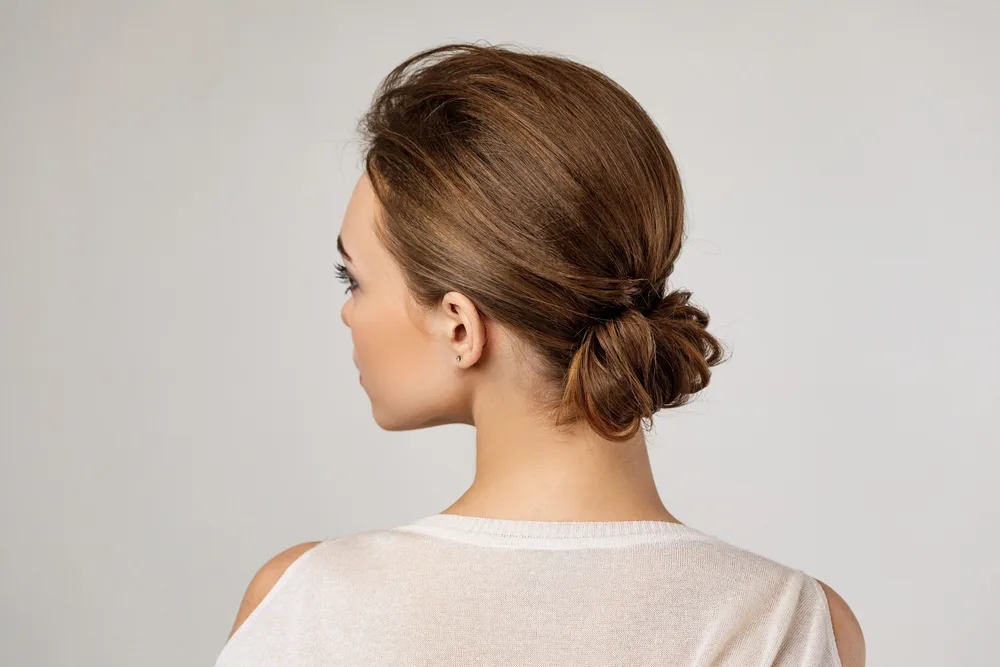 For a piece on medium length layered hairstyles for women over 50, a woman wears a chignon bun and looks left, as seen from behind