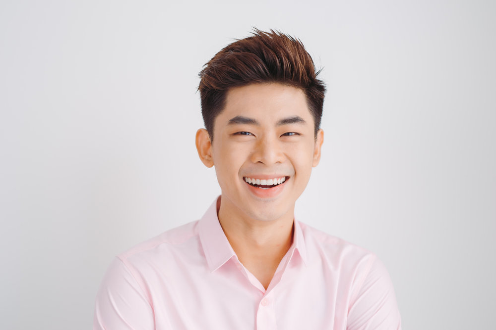 Korean man in light pink collared shirt stands in front of light gray wall with volumized spiky hair, one of the best Korean men hairstyles