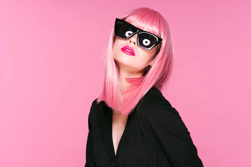 Vibrant Light Watermelon Pink hair on a woman in bulky retro sunglasses in a pink room in a black dress
