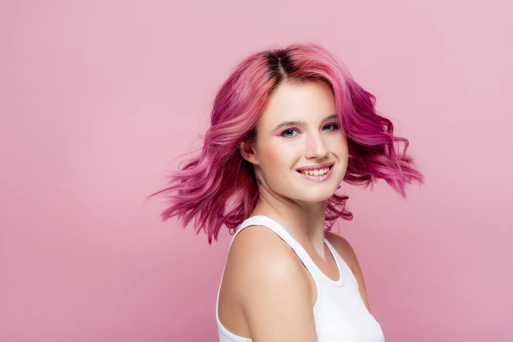 Cute smiling woman with purple hair spinning and standing in front of a pink wall and wearing the Tousled Layers With Medium Curtain Bangs style