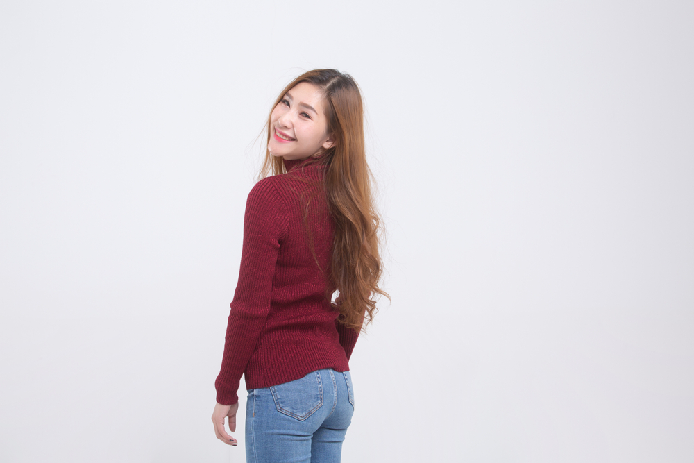 Asian woman stands isolated on white background with red sweater to show off Asian long hair dyed copper with layers