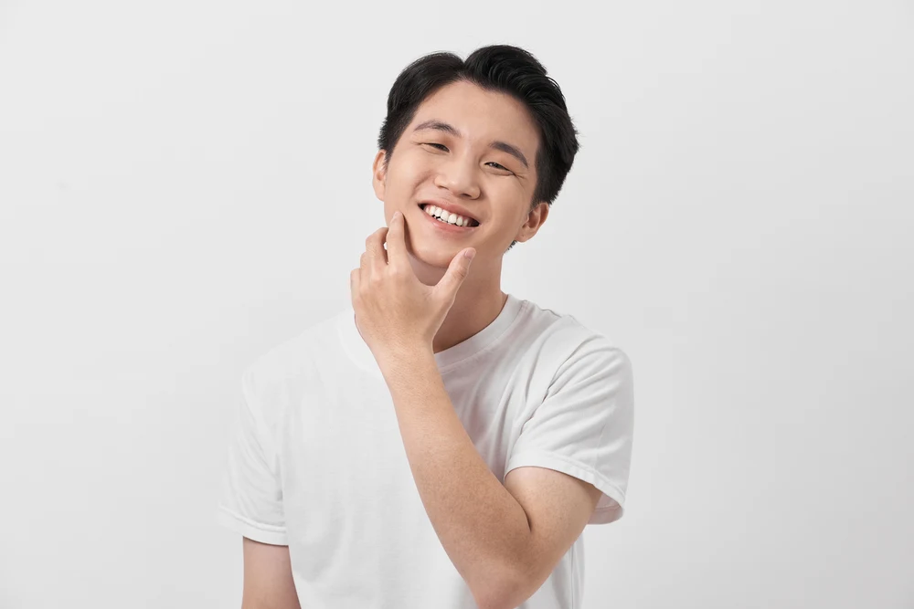 Korean man places his hand on his chin wearing a white t-shirt in a white-walled room with voluminous brushed back hairstyle