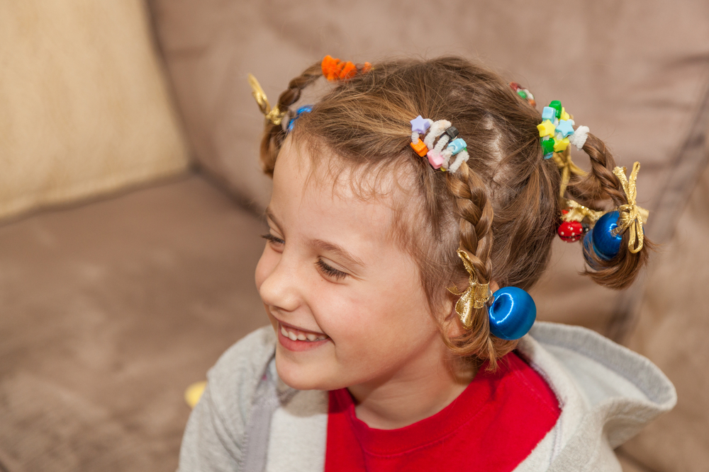 Little girl smiles with closed eyes wearing multiple braids secured with colorful hair accessories for a piece on crazy hair day ideas