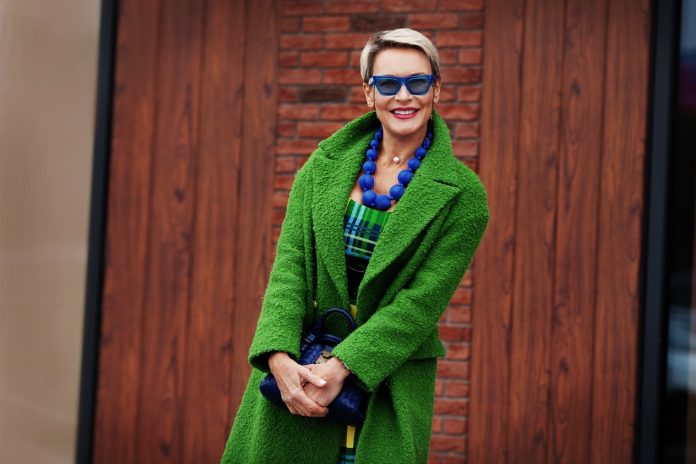 Blonde Pixie With Black Underdye for a piece on black and blonde hair color ideas on a slim woman in a green coat standing in front of a wooden door
