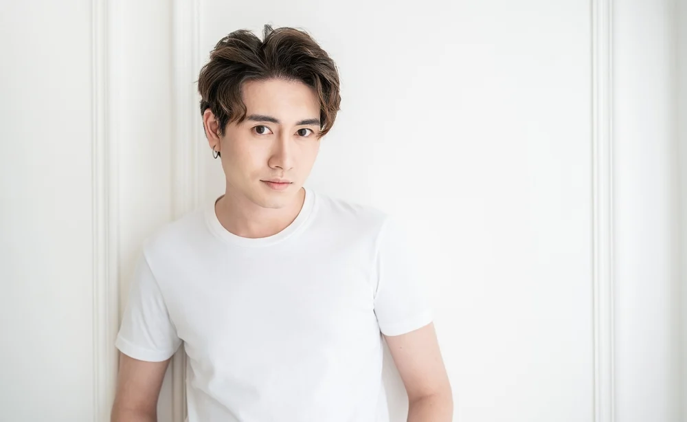 Korean man slightly smiles wearing a white t-shirt in front of white wall with messy side part hairstyle