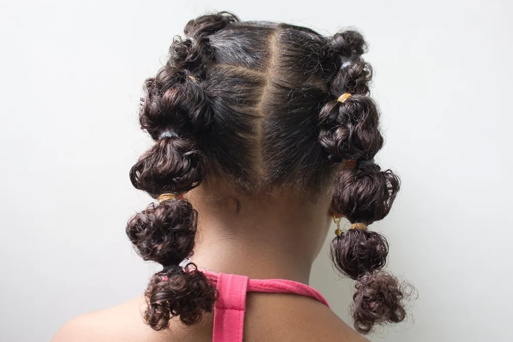 Girl with coily hair shown from the back wearing a flat bubble braid hairstyle with alternating elastics