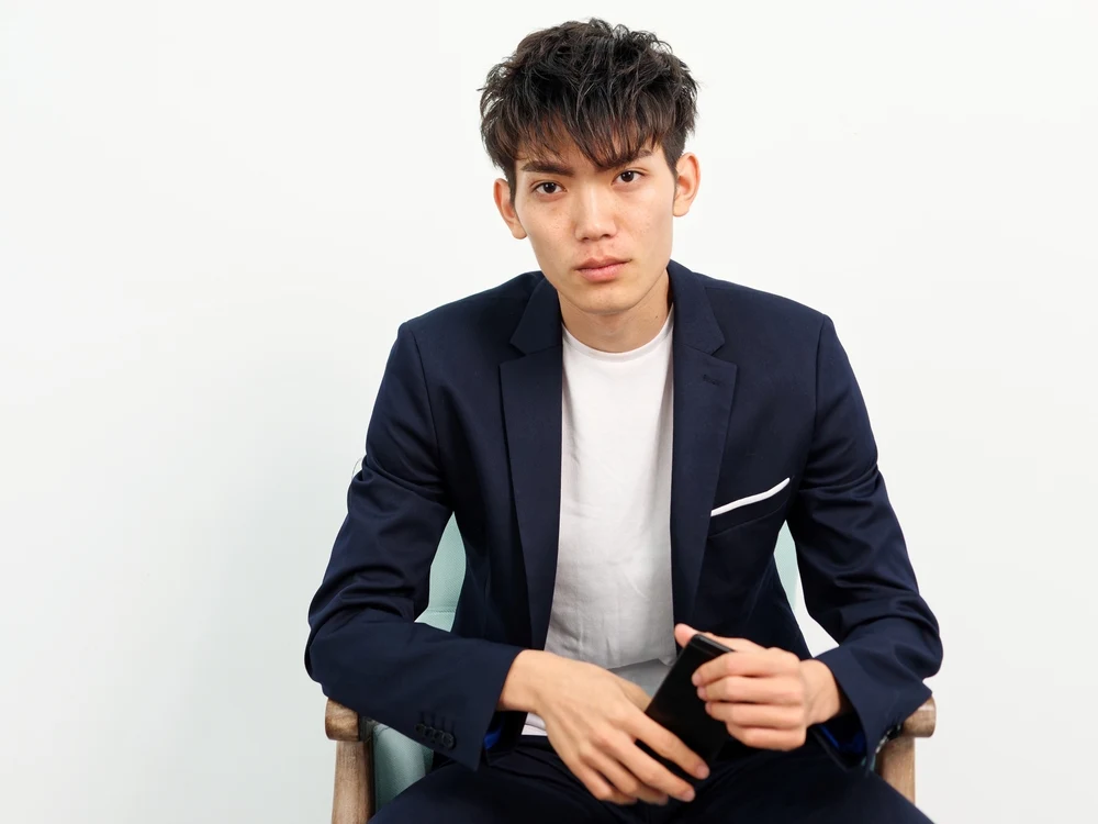 Stylish Korean man in a blazer models a trendy hairstyle with tousled waves and lots of volume brushed forward