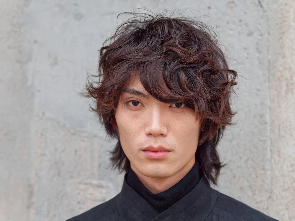 Serious man wears a black high neck shirt with a medium wavy shag hairstyle