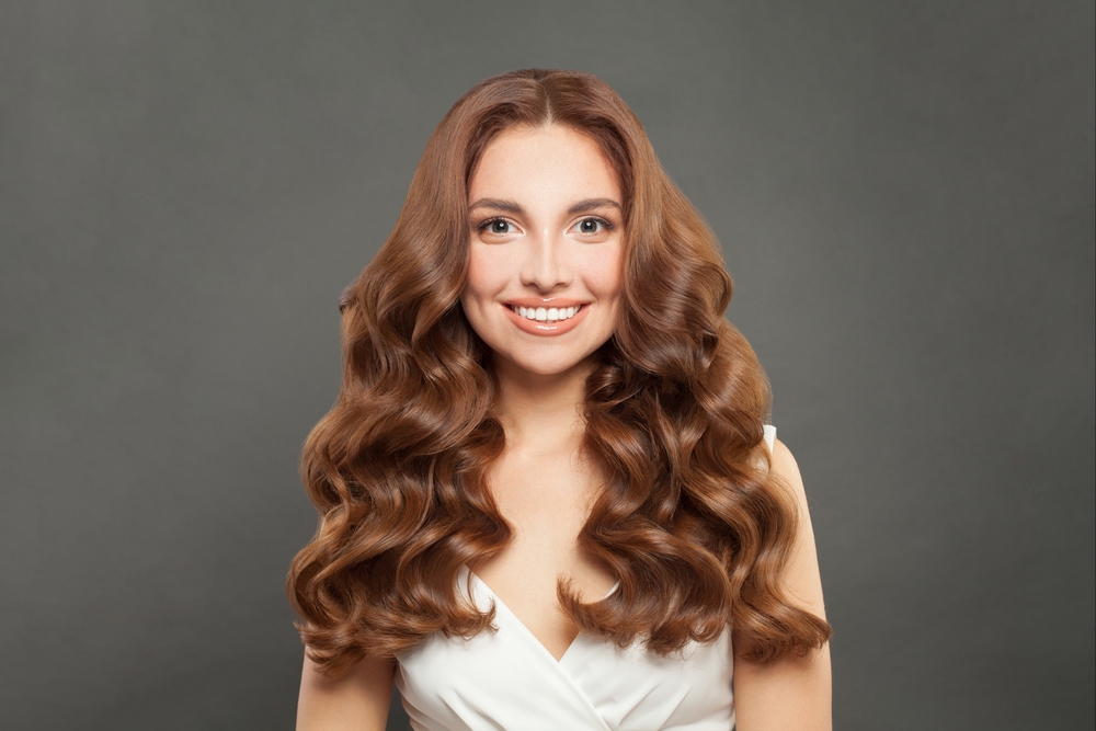 Brunette woman smiles looking straight ahead with voluminous waves and middle part hairstyle