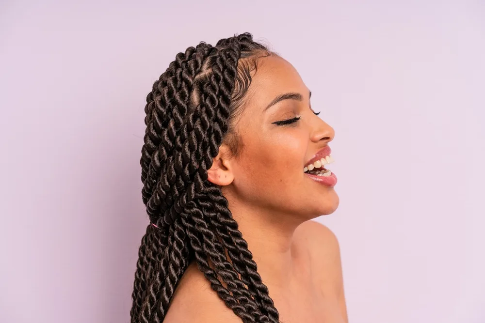 African American woman with bare shoulders laughs in front of a lavender wall with jumbo twists in a half up hairstyle