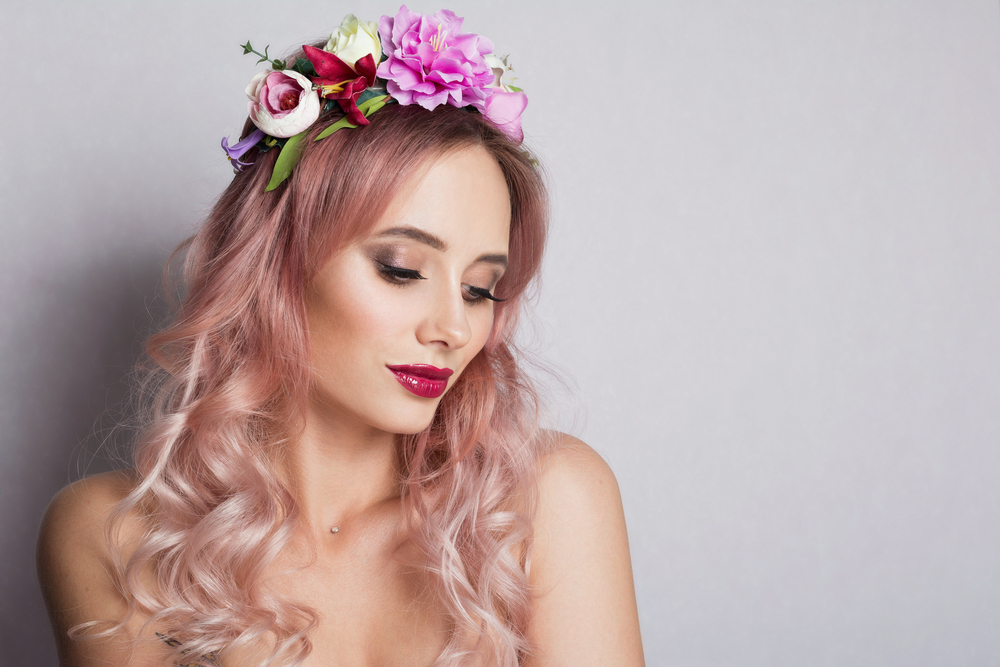 Woman with ombre light pink hair wearing a floral headband, a diamond necklace, and red lipstick in a silver room