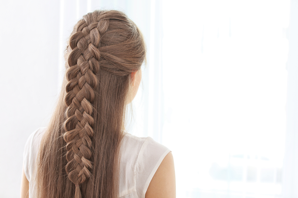Rear view of brunette woman with intricate 5 strand braid half updo standing in front of window