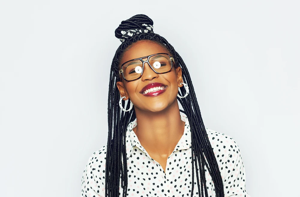 African American woman with glasses and polka dot white top wears hoop earrings and half up half down bun style in front of white background