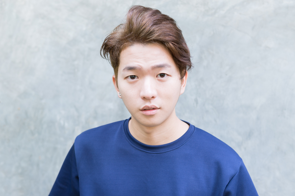 Teenage Korean boy wears a blue sweater in front of a marble wall with a messy Korean men's hairstyle