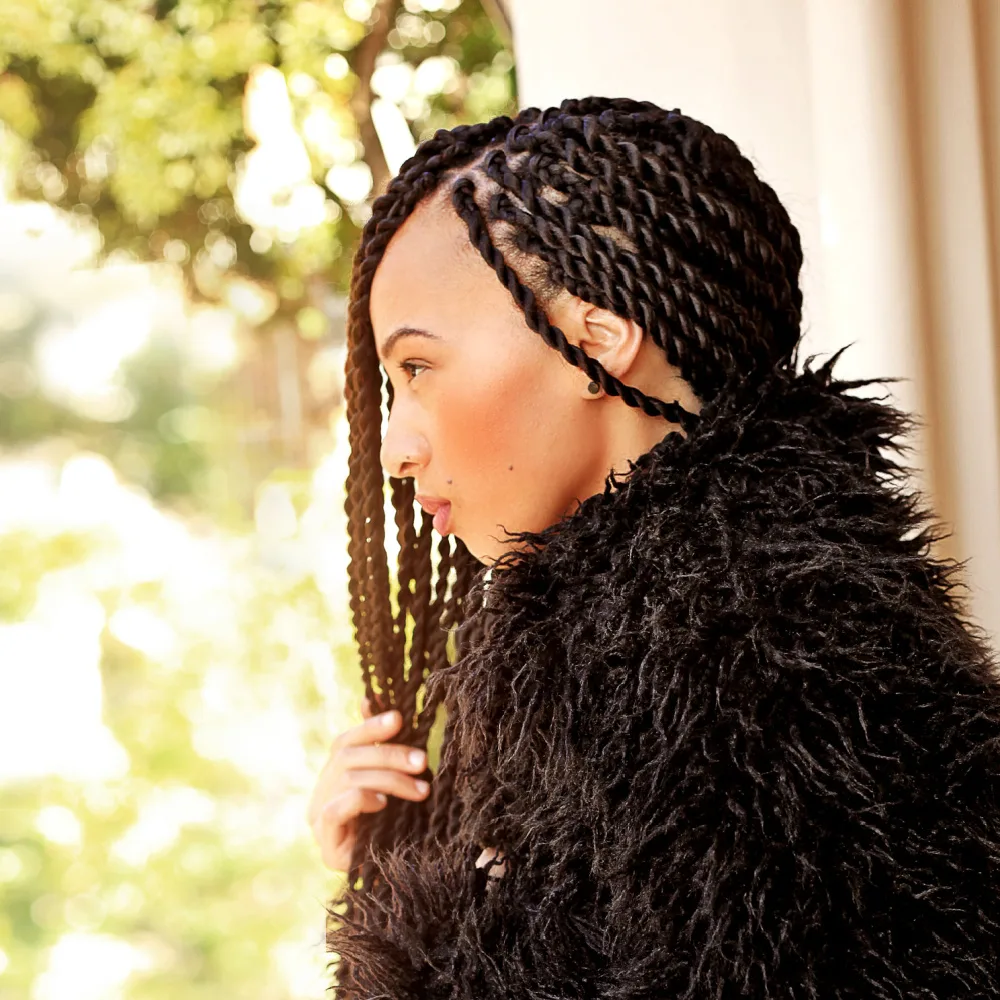 African American woman in fur coat wears a side part spring twist hair style while facing the side outdoors